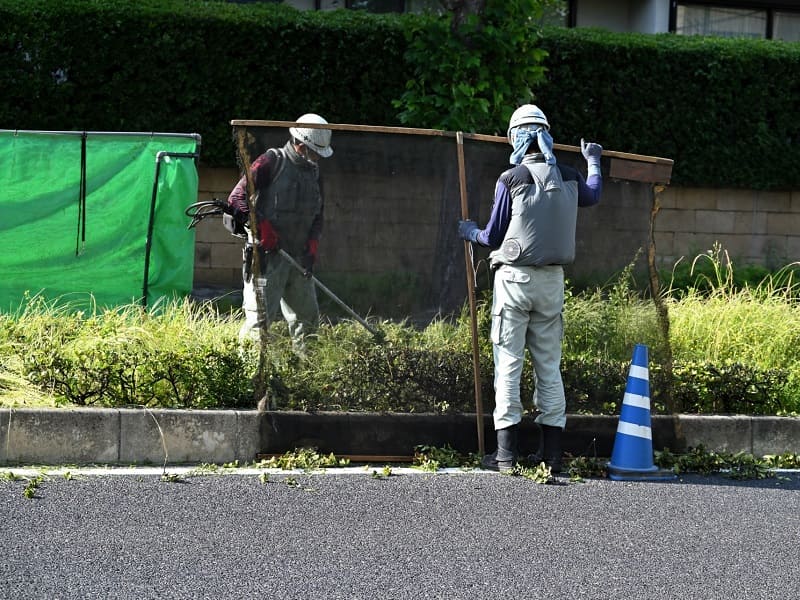 飛散防止ネットを使って草刈りをする人